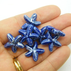 Könnte beinhalten: Sechs blaue Keramik-Seestern-Perlen. Die Perlen sind glänzend und haben eine leicht irisierende Oberfläche.