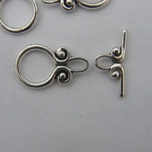 Pu&ograve; includere: Chiusura in metallo argentato con un anello decorativo e una barra a forma di T. L'anello ha due piccole sfere decorative su ogni lato.