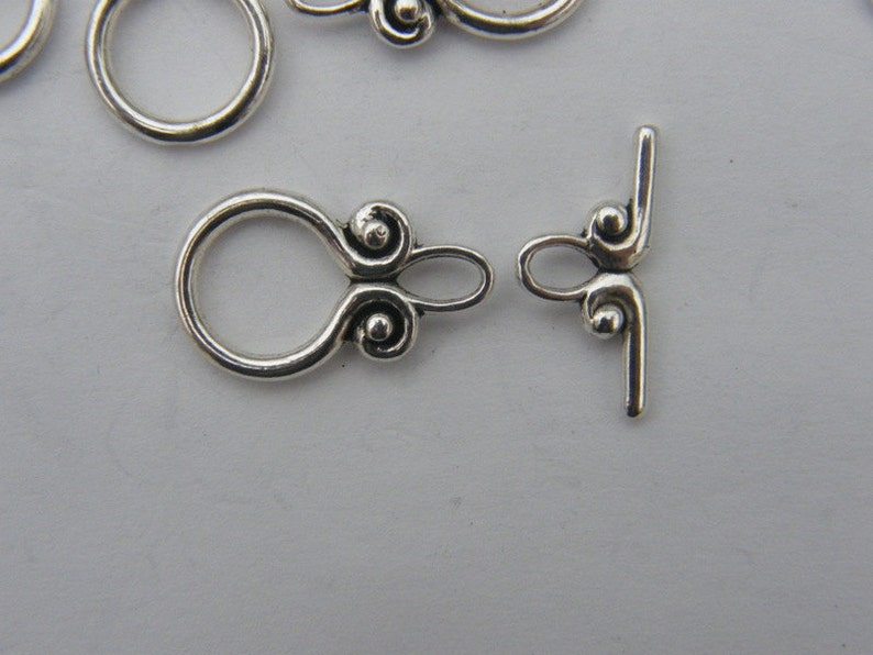 Pu&ograve; includere: Chiusura in metallo argentato con un anello decorativo e una barra a forma di T. L'anello ha due piccole sfere decorative su ogni lato.