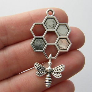 May include: Silver charm featuring a honeycomb design with a small bee pendant. The honeycomb is made of six hexagonal cells.