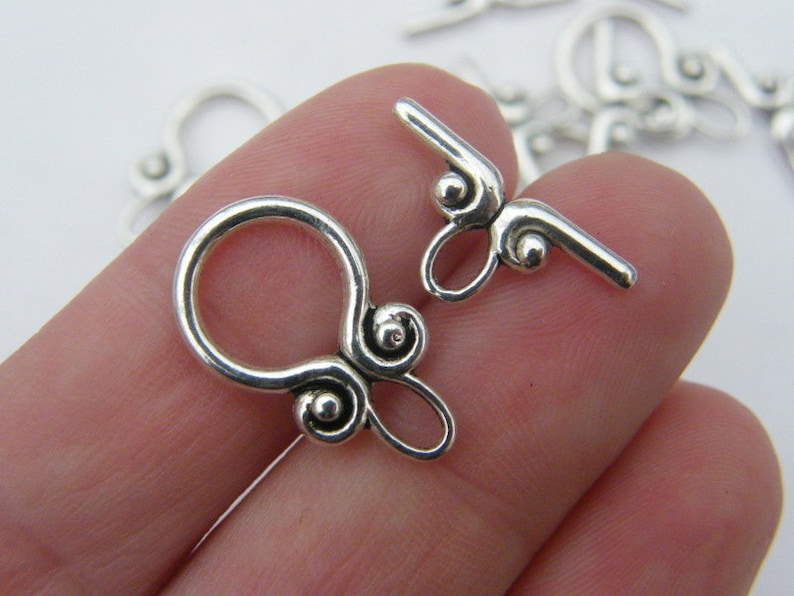 Pu&ograve; includere: Chiusure in metallo argentato con un design a spirale decorativo. Le chiusure sono progettate per essere utilizzate per la creazione di gioielli.