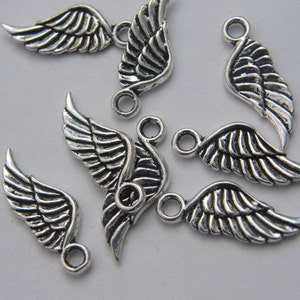 May include: A group of seven silver angel wing charms with a loop at the top for attaching to jewellery or other crafts.