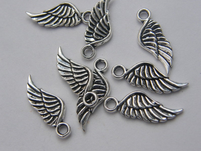 May include: A group of seven silver angel wing charms with a loop at the top for attaching to jewellery or other crafts.