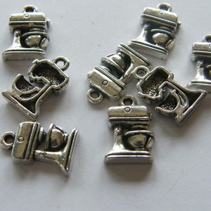 May include: A group of eight silver-toned metal charms shaped like stand mixers. The charms have a loop at the top for attaching to a necklace, bracelet, or other jewelry.