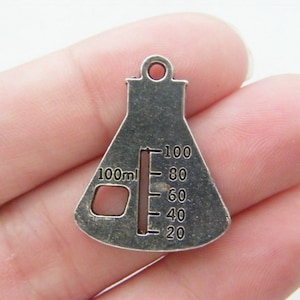 Può includere: Ciondolo in metallo color argento a forma di becher con una marcatura di 100 ml e una scala graduata da 20 a 100.