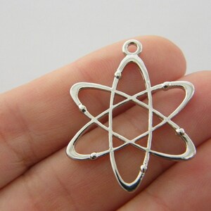 Op de afbeelding: Een zilverkleurige atoombedel met een lus aan de bovenkant om aan een ketting of armband te bevestigen. De bedel heeft een centrale kern met draaiende ringen en kleine kraalachtige details. Het ontwerp is een weergave van een atoom.