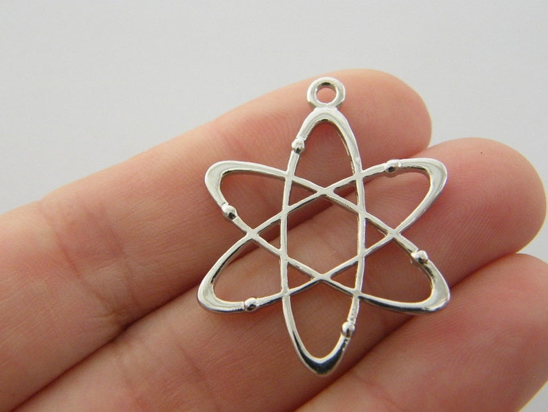 Op de afbeelding: Een zilverkleurige atoombedel met een lus aan de bovenkant om aan een ketting of armband te bevestigen. De bedel heeft een centrale kern met draaiende ringen en kleine kraalachtige details. Het ontwerp is een weergave van een atoom.