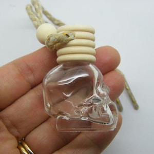 Puede incluir: Una botella de vidrio transparente con forma de cráneo con una tapa de madera y una cuerda atada. La botella está siendo sostenida en una mano.