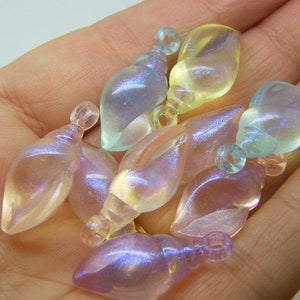 Pode incluir: Uma coleção de pingentes em forma de concha de mar iridescentes em várias cores pastel, incluindo rosa, azul e amarelo. Os pingentes têm um acabamento brilhante e perolado e são perfeitos para fazer joias ou artesanato.