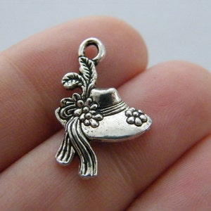 May include: Silver charm in the shape of a hat with a flower detail. The charm has a loop at the top for attaching to a bracelet or necklace.