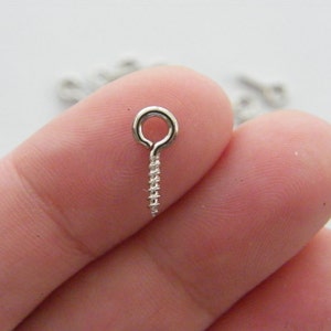 May include: Silver screw-in eyelet with a small loop at the top. The eyelet is held in a person's hand.