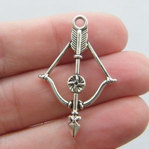 May include: Silver charm in the shape of a bow and arrow. The arrow has a feathered fletching and the bow has a circular design in the center.