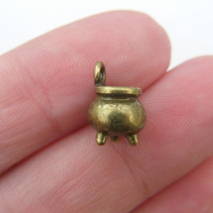 Puede incluir: Un pequeño amuleto de metal dorado antiguo en forma de caldero. El amuleto tiene un bucle en la parte superior para sujetarlo a un collar o pulsera.