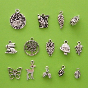 May include: A collection of 16 silver charm pendants featuring nature-inspired designs, including a tree, owl, mushroom, acorn, butterfly, rabbit, deer, and leaves.