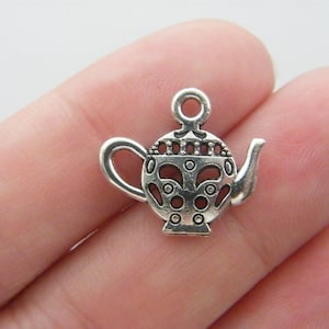May include: Silver charm in the shape of a teapot with an ornate design. The charm has a loop at the top for attaching to a necklace or bracelet.