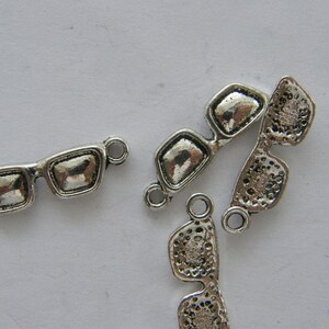 May include: Silver-toned metal charms shaped like sunglasses. The charms have a loop at the top for attaching to jewelry or other crafts.