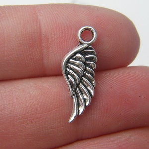 May include: Silver-toned metal charm in the shape of an angel wing. The wing has a detailed design with a textured surface.