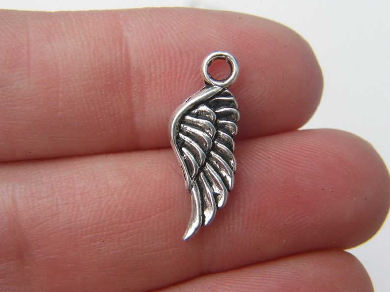 May include: Silver-toned metal charm in the shape of an angel wing. The wing has a detailed design with a textured surface.