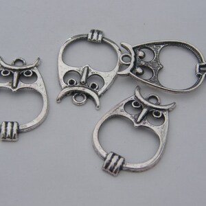 May include: Four silver owl-shaped charms with open centers. The charms have intricate details and are perfect for jewelry making.
