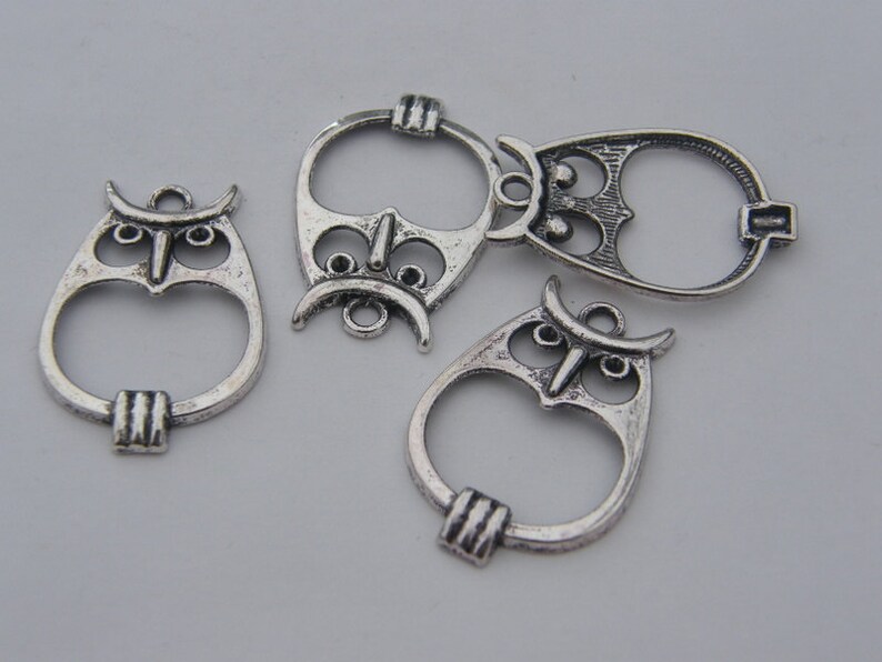 May include: Four silver owl-shaped charms with open centers. The charms have intricate details and are perfect for jewelry making.