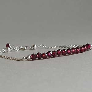 May include: A delicate silver chain bracelet with a single row of deep red garnet beads.