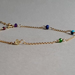 May include: A gold chain bracelet with seven colourful gemstone beads. The beads are orange, red, purple, blue, turquoise, green, and yellow.
