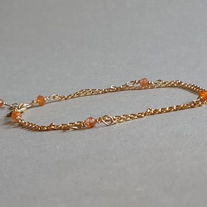 Può includere: Un braccialetto delicato a catena dorata con piccole perle di pietre preziose arancioni.