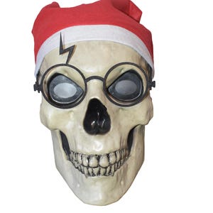 May include: A white skull mask with a black nose and mouth, wearing round black glasses with a lightning bolt sticker on the forehead. The skull is wearing a red Santa hat with a white trim.