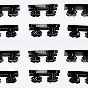 May include: Twelve black plastic furniture feet with a rectangular base and two rounded protrusions on top.