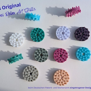 Könnte beinhalten: Eine Sammlung kreisförmiger, stacheliger Kunststoffscheiben in verschiedenen Farben wie Weiß, Türkis, Lila, Grau, Pink, Blau und Pfirsich. Der Text "Das Original nur bei Relax Art Skills" und "beim Deutschen Patent- und Markenamt eingetragener Designschutz" ist sichtbar.