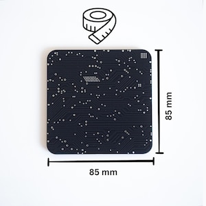 Pode incluir: Uma placa de circuito quadrada, azul marinho escuro, com cantos arredondados, medindo 8,5 cm de cada lado. A placa apresenta um padrão complexo de traços e componentes de circuito brancos. Uma ilustração em preto e branco de uma fita métrica está no canto superior esquerdo.