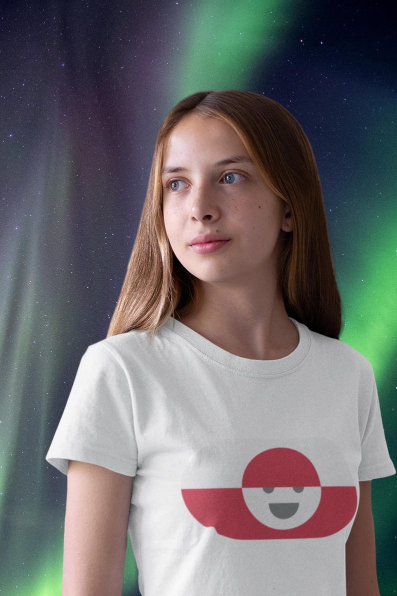 Peut inclure: T-shirt blanc avec un motif graphique d'un cercle rouge sur une forme horizontale rouge et blanche avec un visage souriant. Le t-shirt est port&eacute; par une personne aux longs cheveux bruns, sur fond de ciel &eacute;toil&eacute; aux teintes vertes et violettes.