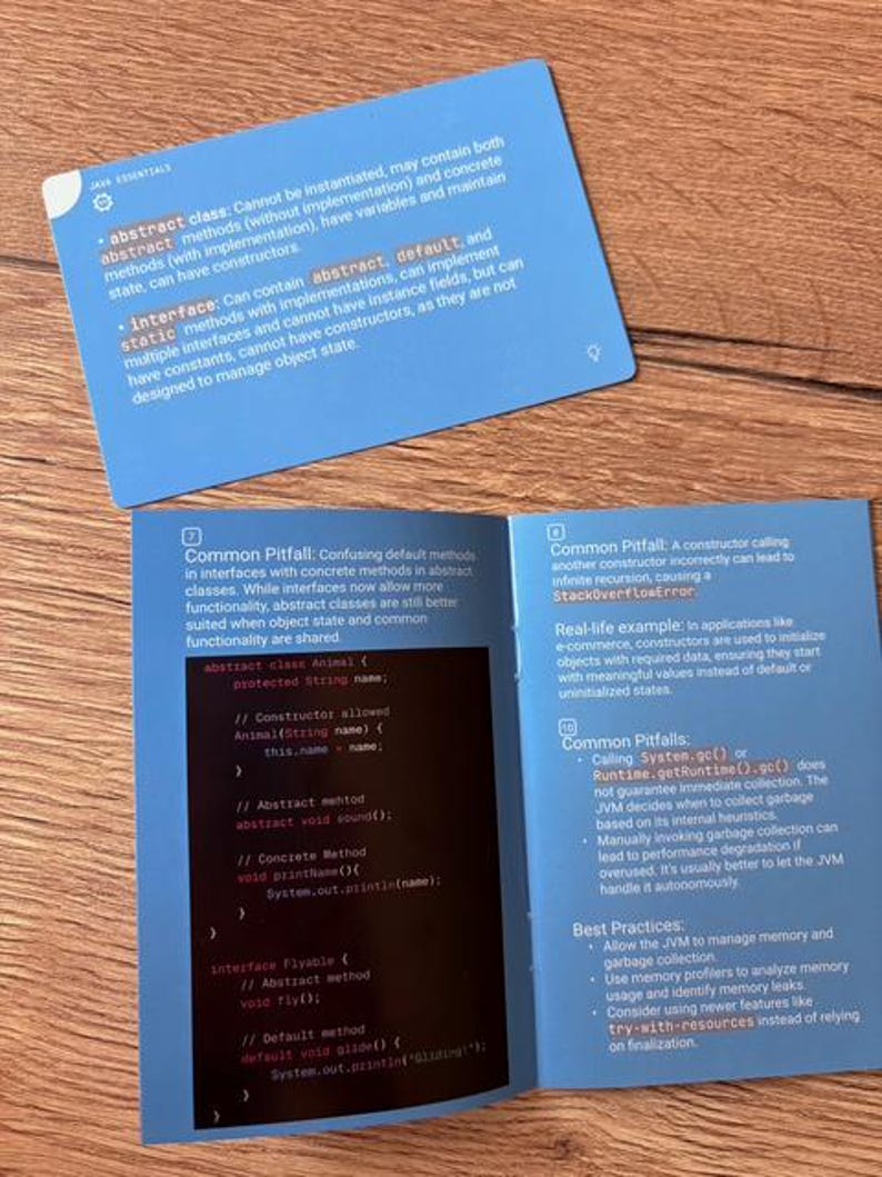 Puede incluir: Libro abierto y tarjeta con texto sobre conceptos de programaci&oacute;n Java. Las tarjetas azules y las p&aacute;ginas del libro muestran informaci&oacute;n sobre clases abstractas, interfaces y trampas comunes. El libro tambi&eacute;n muestra ejemplos de c&oacute;digo.