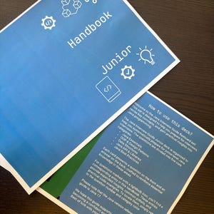 Puede incluir: Dos manuales azules con texto y gr&aacute;ficos blancos. El manual superior dice "Handbook Junior" con iconos. El segundo manual tiene texto sobre la preparaci&oacute;n de entrevistas de Java, incluyendo categor&iacute;as.