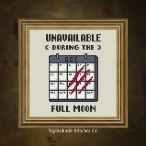 May include: A framed cross-stitch design featuring the text "UNAVAILABLE DURING THE" above a pixelated calendar marked "OCT" with red slashes and the words "FULL MOON" below. The frame is gold-toned.
