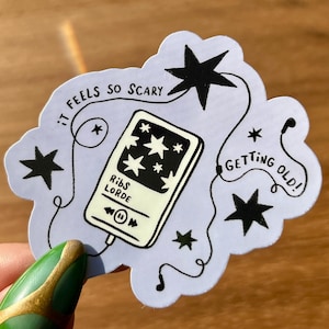 May include: A sticker with a light purple background featuring a black and white illustration of a music player with stars. The text "It feels so scary" and "Getting old!" are written on the sticker. The music player displays the text "Ribs Lorde".