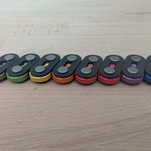 May include: A collection of eight key organizers in various colors, including bronze, green, gold, orange, red, pink, purple, and blue. Each organizer has a black body with two silver-colored circular accents.