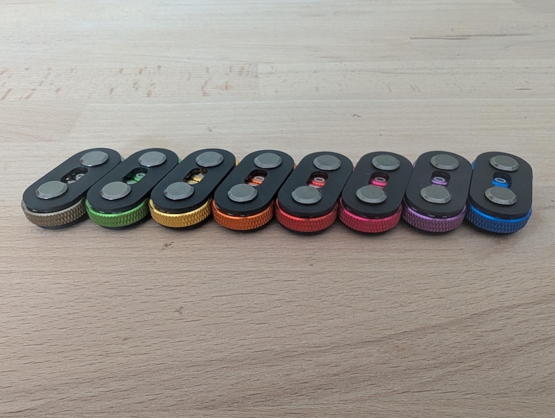 May include: A collection of eight key organizers in various colors, including bronze, green, gold, orange, red, pink, purple, and blue. Each organizer has a black body with two silver-colored circular accents.