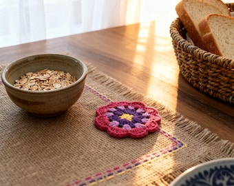 Può includere: Una tavola rustica per la colazione con un cestino di pane a fette, una ciotola di ceramica piena di avena e un sottobicchiere all'uncinetto fatto a mano nei toni del rosa, viola e giallo. Il sottobicchiere è su un runner di iuta.