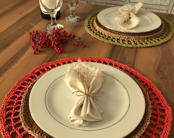 Può includere: Una tavola apparecchiata con piatti bianchi, tovaglioli beige e rametti decorativi. I piatti poggiano su tovagliette all'uncinetto rosse, marroni e verdi. Sono visibili anche calici e una bottiglia di vino, creando un'atmosfera calda.