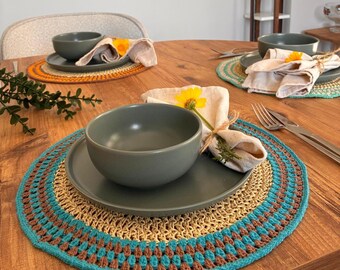 Può includere: Tavola apparecchiata con un sottobicchiere all'uncinetto fatto a mano in turchese, marrone e beige. L'allestimento comprende un piatto grigio, una ciotola grigia, un tovagliolo di lino piegato e un fiore giallo. Posate visibili.