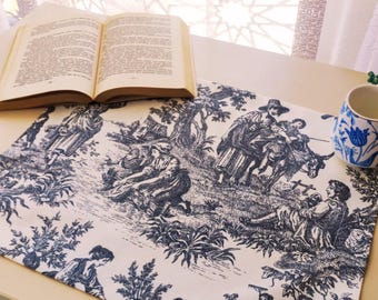 Può includere: Una tovaglia in toile de Jouy blu e bianca con una scena pastorale con figure, alberi e animali. Un libro aperto e una tazza da tè floreale blu e bianca sono sul tavolo. La tovaglia è in tessuto.