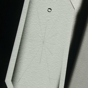 May include: A clear glass octagon-shaped pendant with a hole in the center and a starburst design etched on the surface.