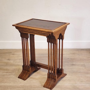 May include: A small, rectangular wooden side table with a dark brown top and intricate column-like legs. The table is made of a light brown wood and features a decorative design. The table is approximately 24 inches tall.