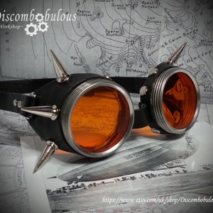May include: A pair of steampunk goggles with orange lenses, black leather straps, and silver metal accents. The goggles have multiple spikes on the sides and are set against a map background.