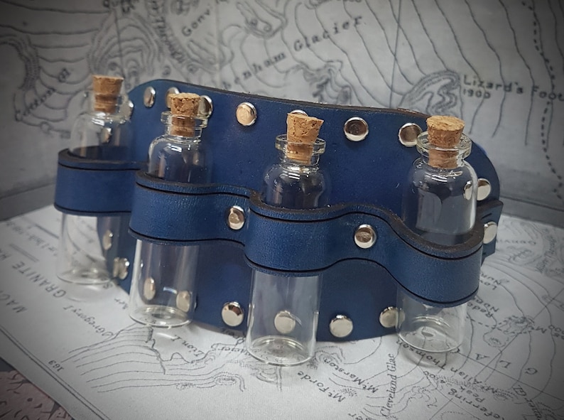 May include: A blue leather wristlet with four small glass bottles with cork stoppers. The wristlet has silver metal rivets and is designed to hold small vials.