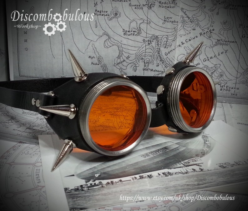May include: A pair of steampunk goggles with orange lenses, black leather straps, and silver metal accents. The goggles have multiple spikes on the sides and are set against a map background.