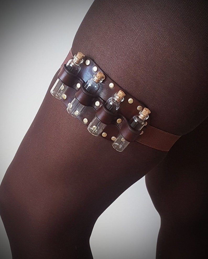May include: A brown leather garter with six small glass vials attached. The vials have cork stoppers and are held in place by metal rivets. The garter is decorated with gold-colored studs.