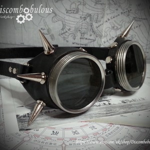 May include: Black leather steampunk goggles with silver accents and spikes. The goggles have round lenses and a black leather strap.