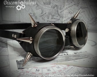 Może przedstawiać: Okulary steampunk ze skóry w kolorze czarnym z srebrnymi akcentami i kolcami. Okulary mają okrągłe szkła i czarny skórzany pasek.